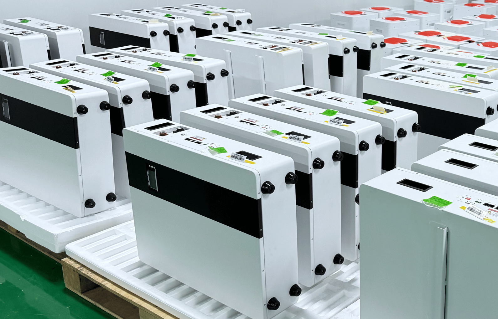 Rader av vita energilagringsmoduler står uppradade på pallar i en ljus fabriksmiljö.