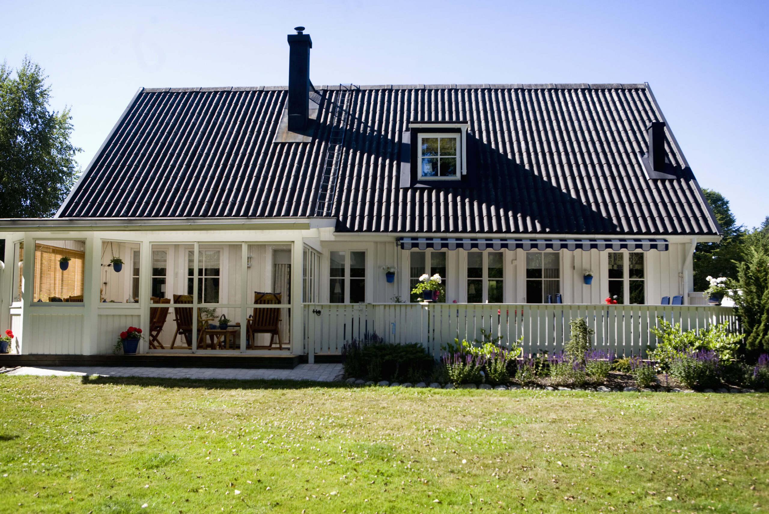 Ett vitt hus baksida med svart tak vid gräsmatta.